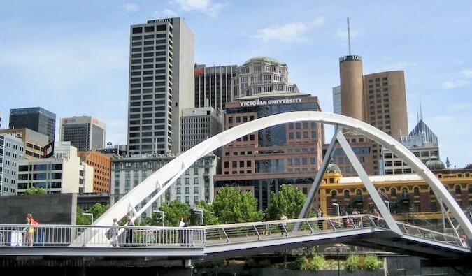 The Melbourne skyline as seen behind an arched pedestrian bridge over the Yarra River